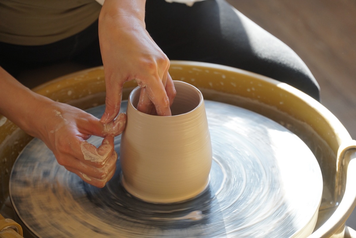 Close-up of hands pulling a handle on a pottery piece
