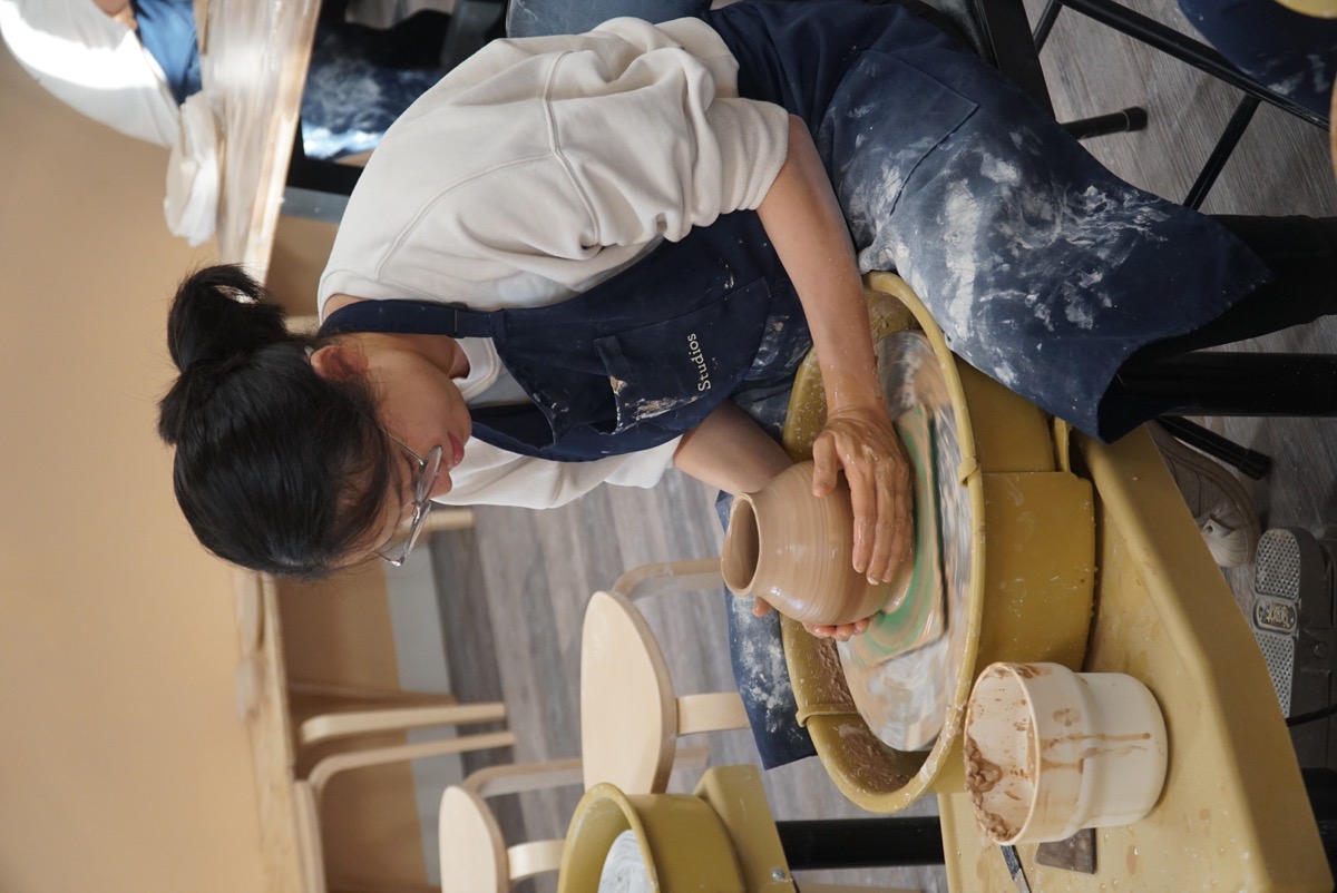 Student in Olomana Studios apron throwing pottery on the wheel