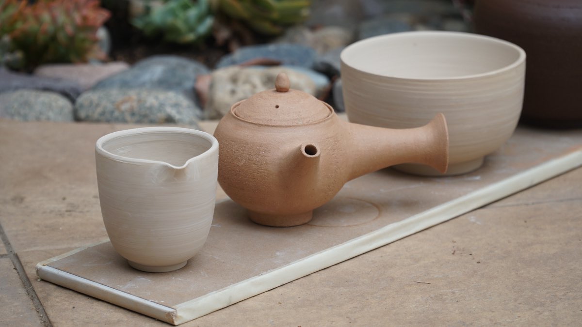 Handmade teapot and cups displayed on a board