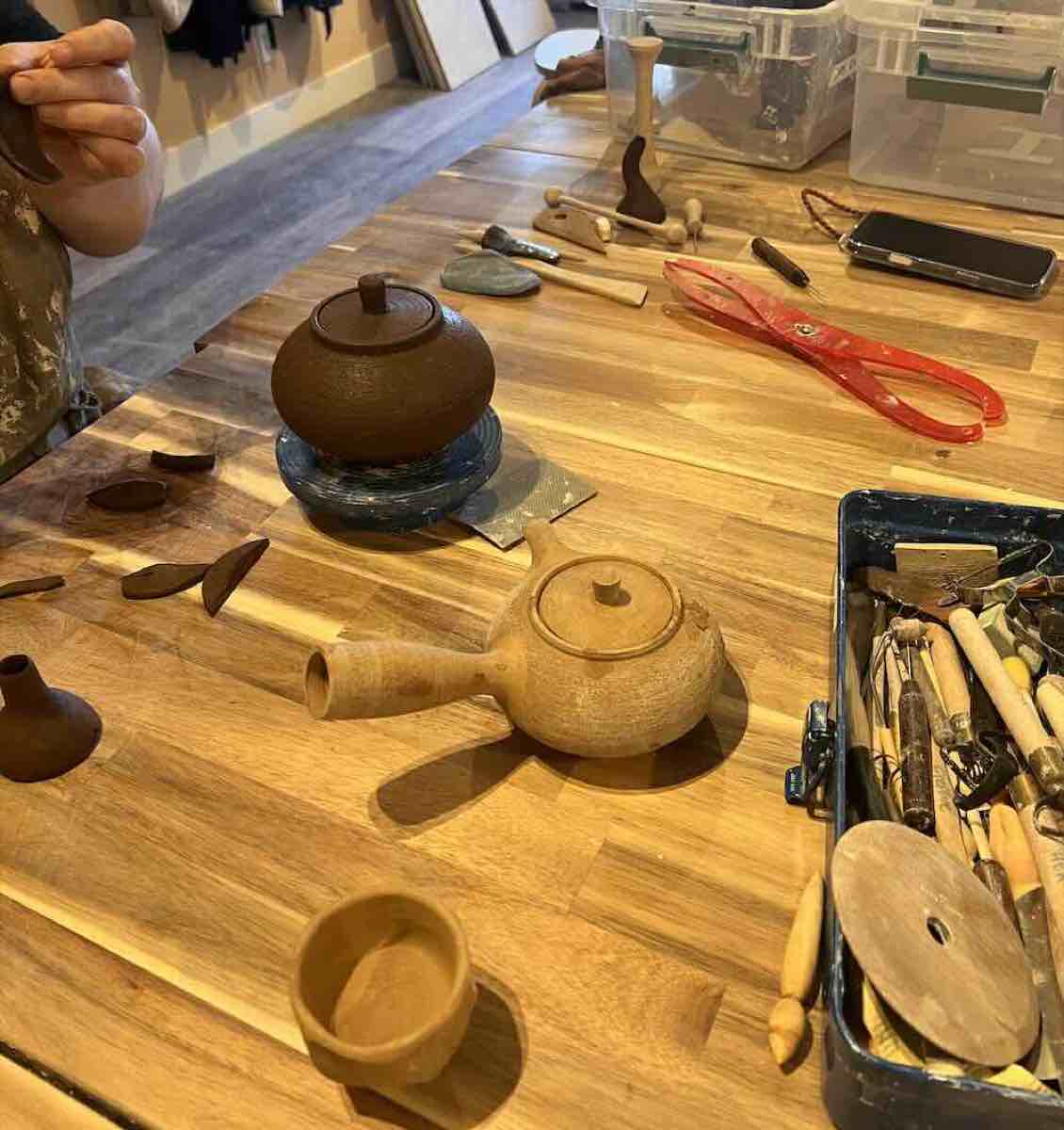 Teapots and yunomi cups on the workbench with pottery tools